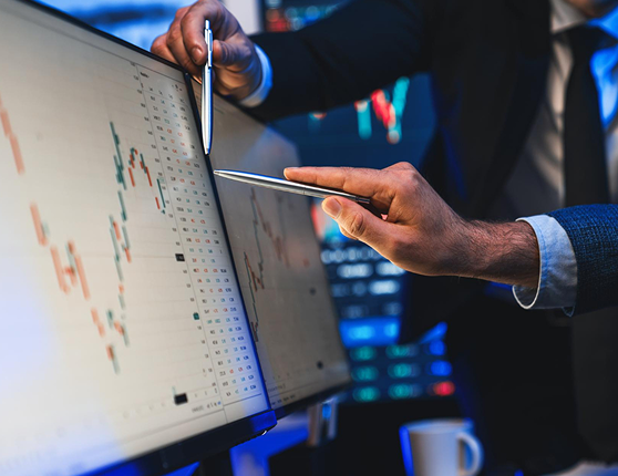 Two people pointing at financial charts on screens
